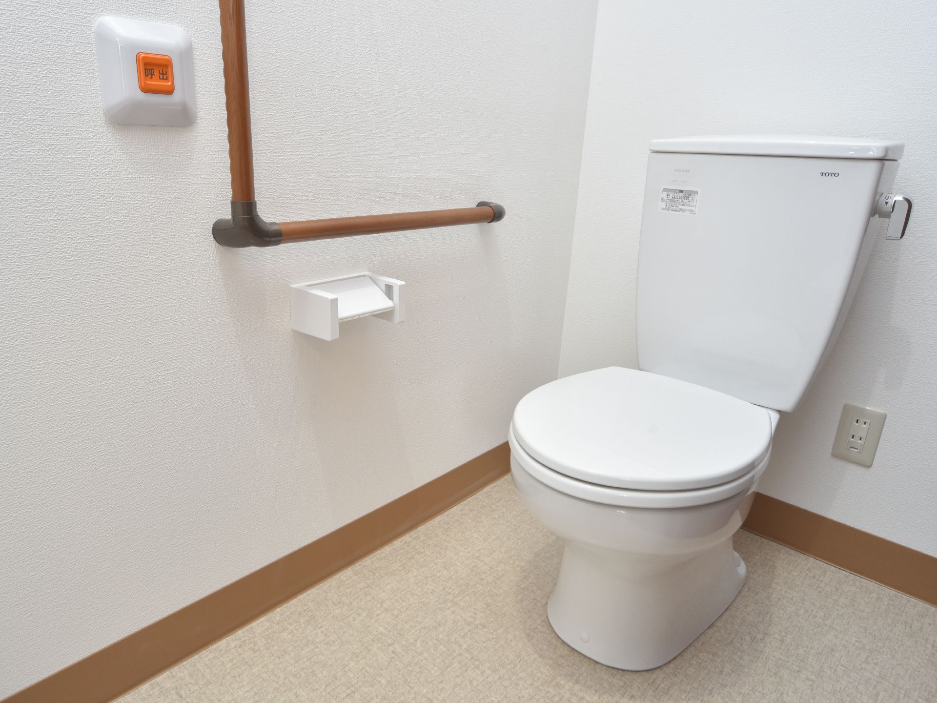 トイレの壁に手すりと急な体調不良時等に使用できるボタンを完備している。トイレの奥にコンセントが2口ある。