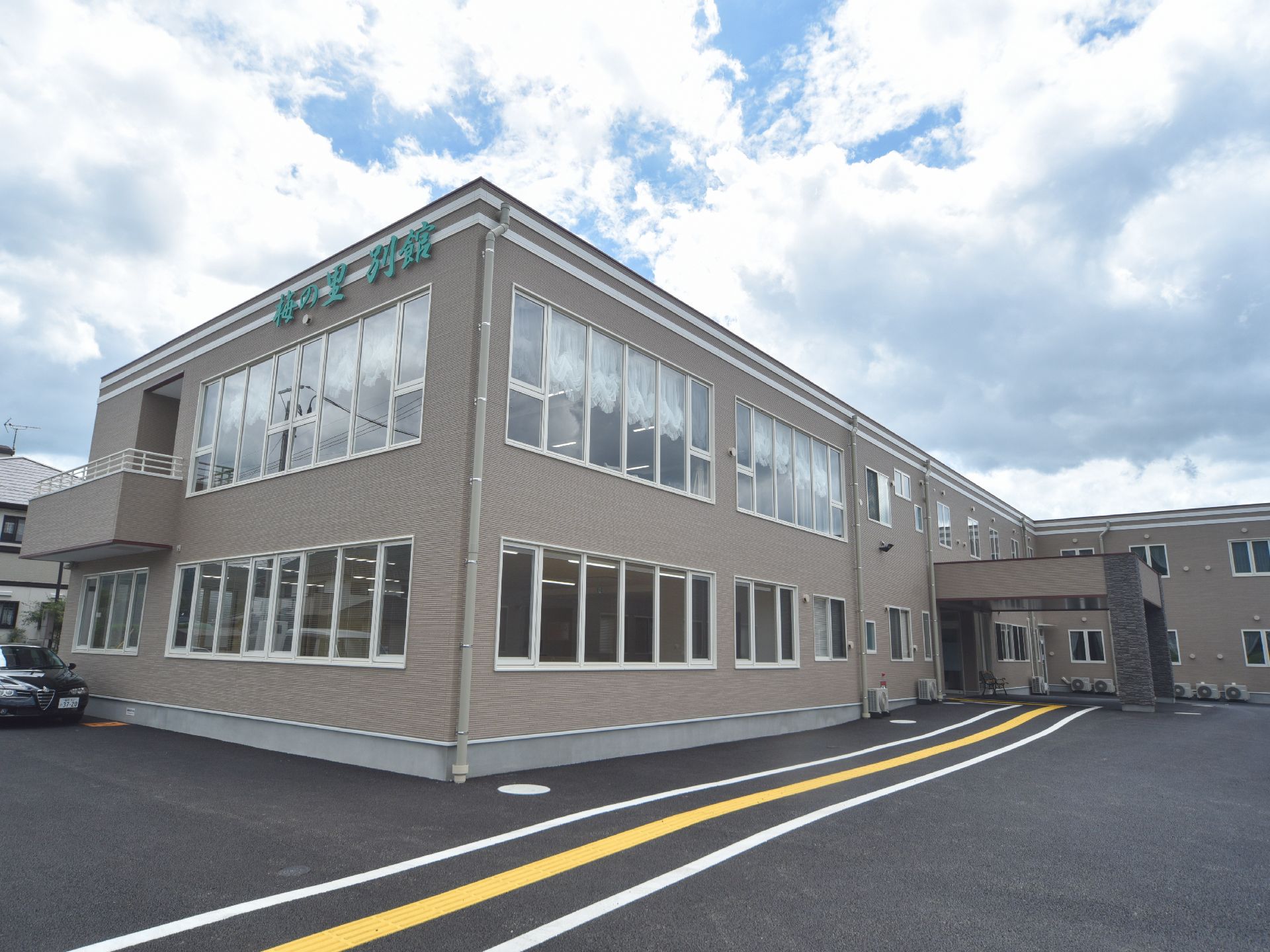 施設はグレーの2階建ての建物。施設の名称が建物に掲示されている。敷地内はアスファルトで整地されている。