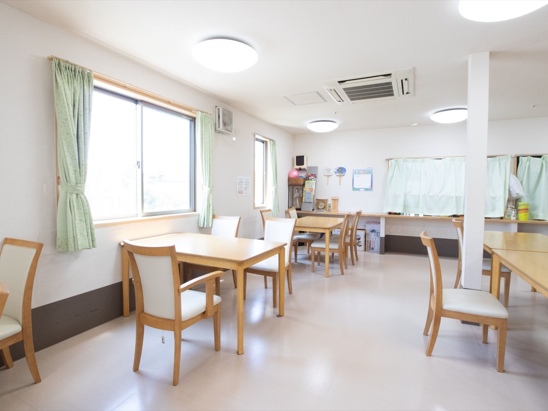 天井に蛍光灯色のシーリングライトと埋め込み型のエアコンが設置されている。壁に換気扇が設置され、うちわが飾られている。