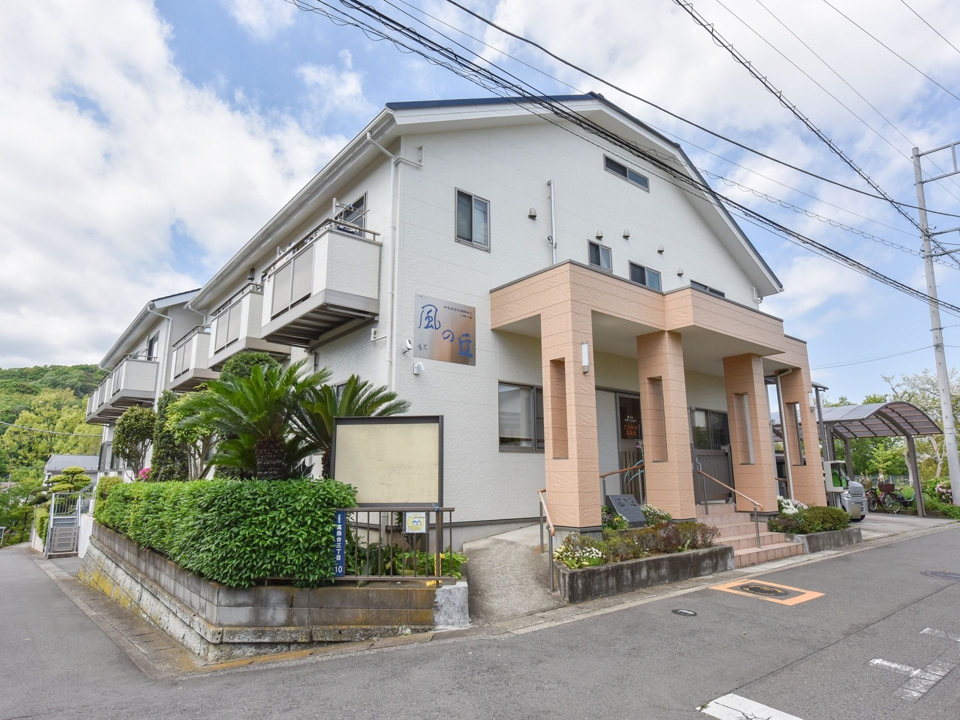 施設建物は坂のある場所に建てられている。植え込みの植物はよく手入れされ、フェンスを覆って生垣のようになっている。