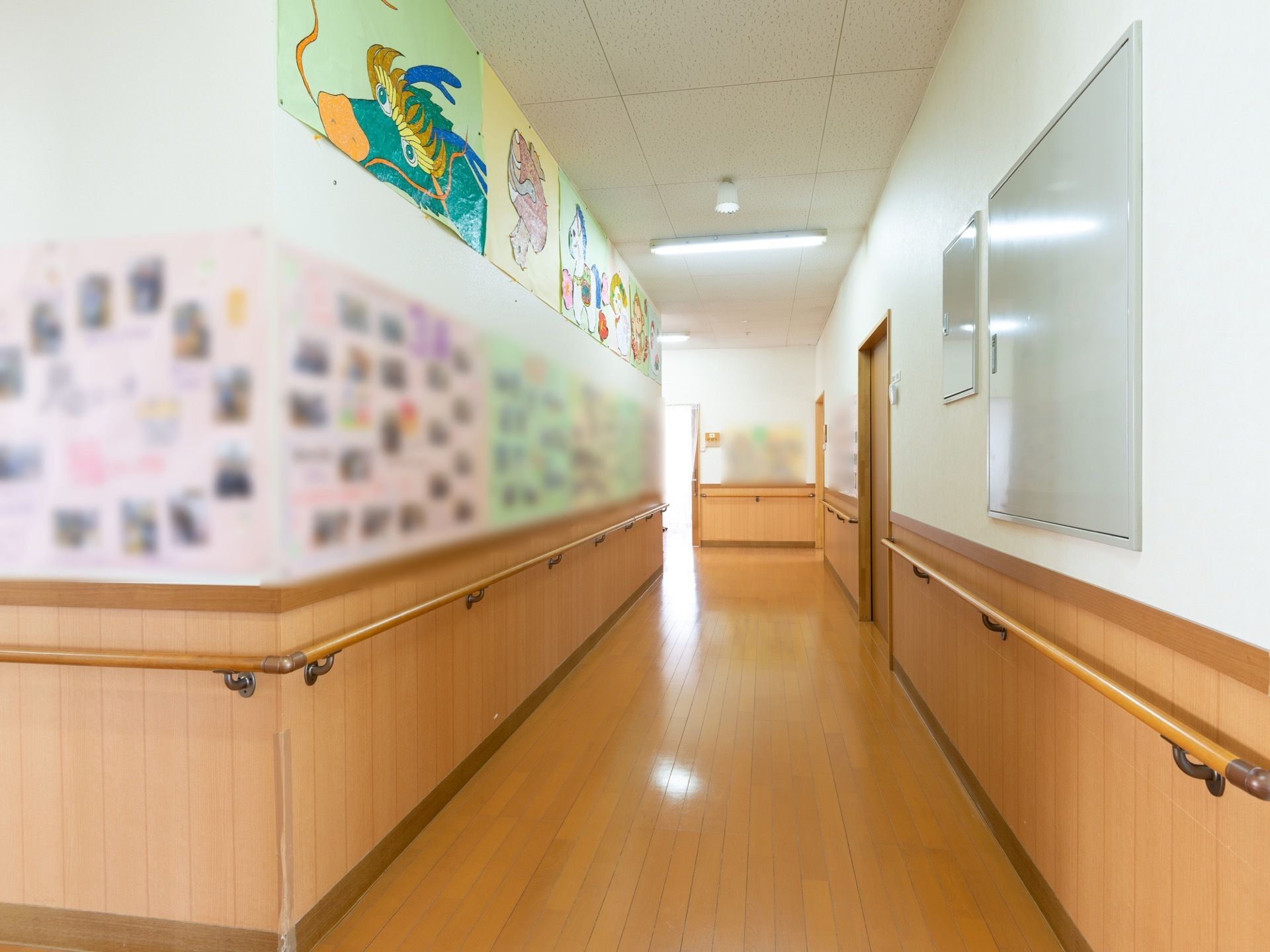通路幅が広々とした廊下である。壁には手すりが備わっており、入居者様が製作した作品や写真が飾られている。照明が設置されている。