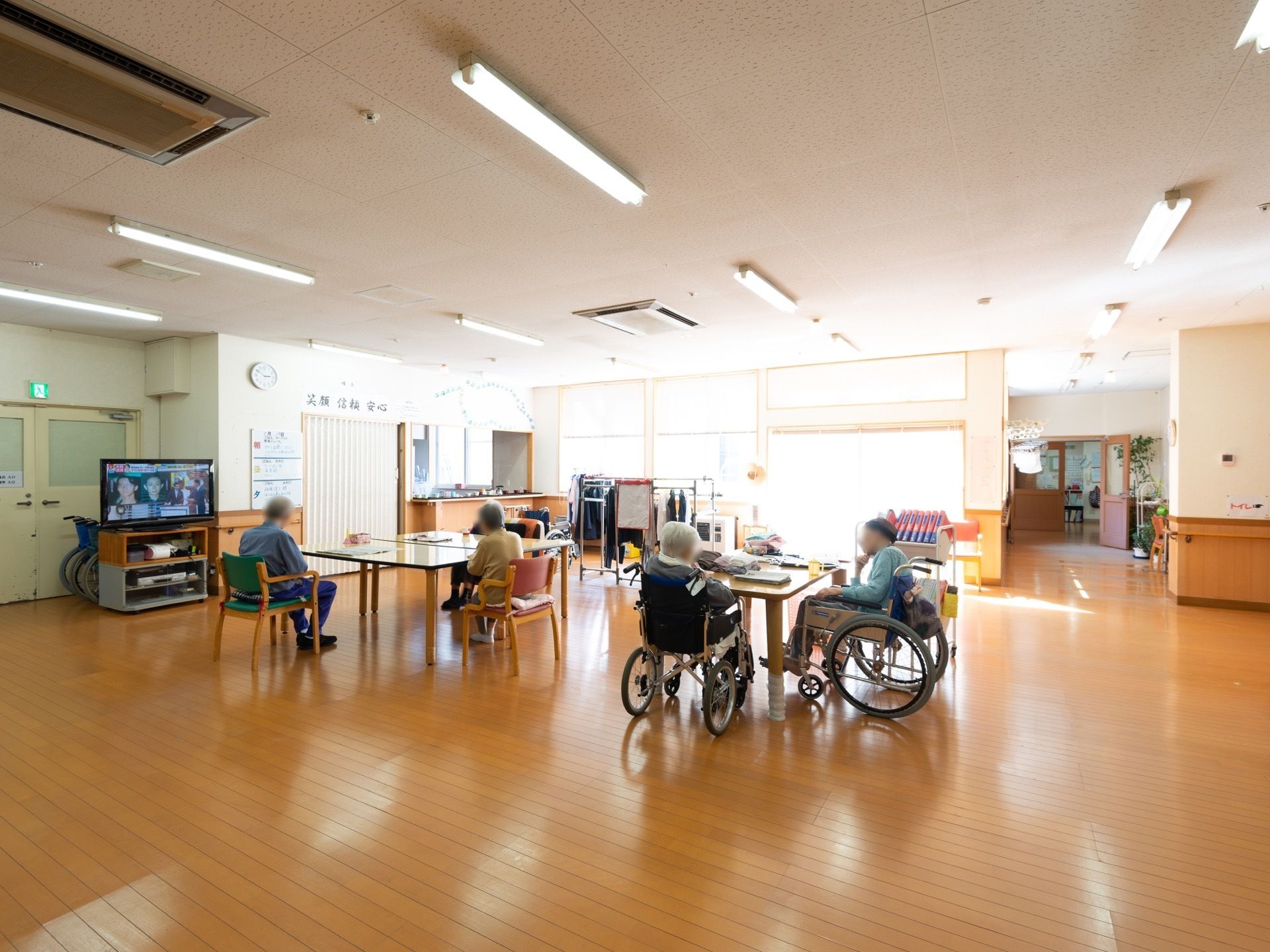 広々とした共有スペースには入居者様が集い思い思いに過ごしている。床はフローリングになっており、部屋の奥にキッチンが併設されている。