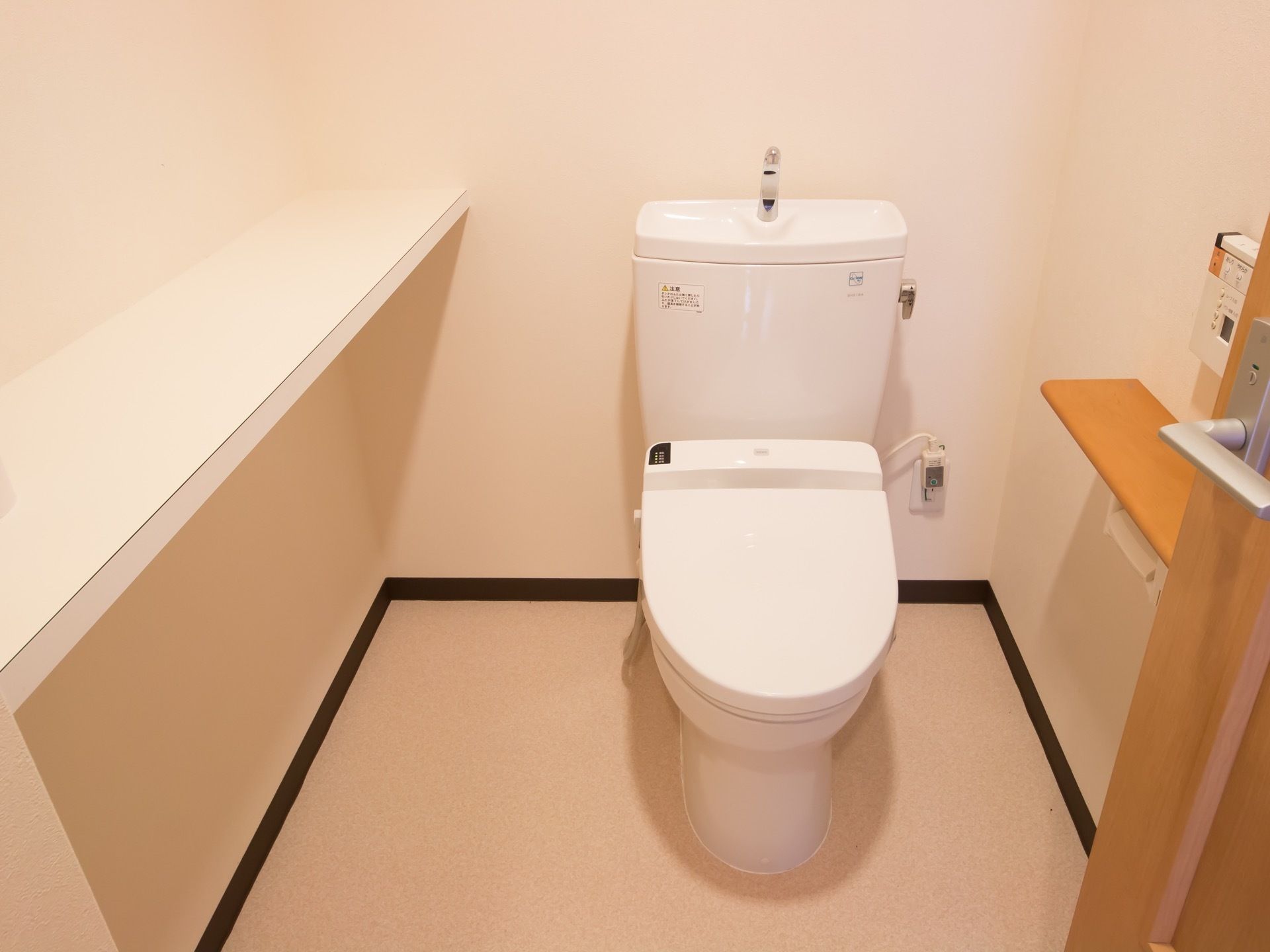 白を基調としたトイレで、隅々まで清掃が行き届いている。洋式便座である。壁側には白色の棚が設置されている。