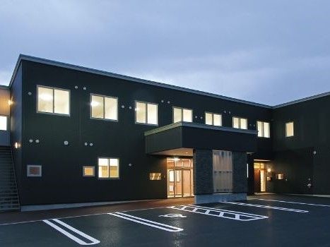 こげ茶色が基調になった２階建ての建物。周辺が少し暗くなっている中、建物内の明かりがとても目立っている。