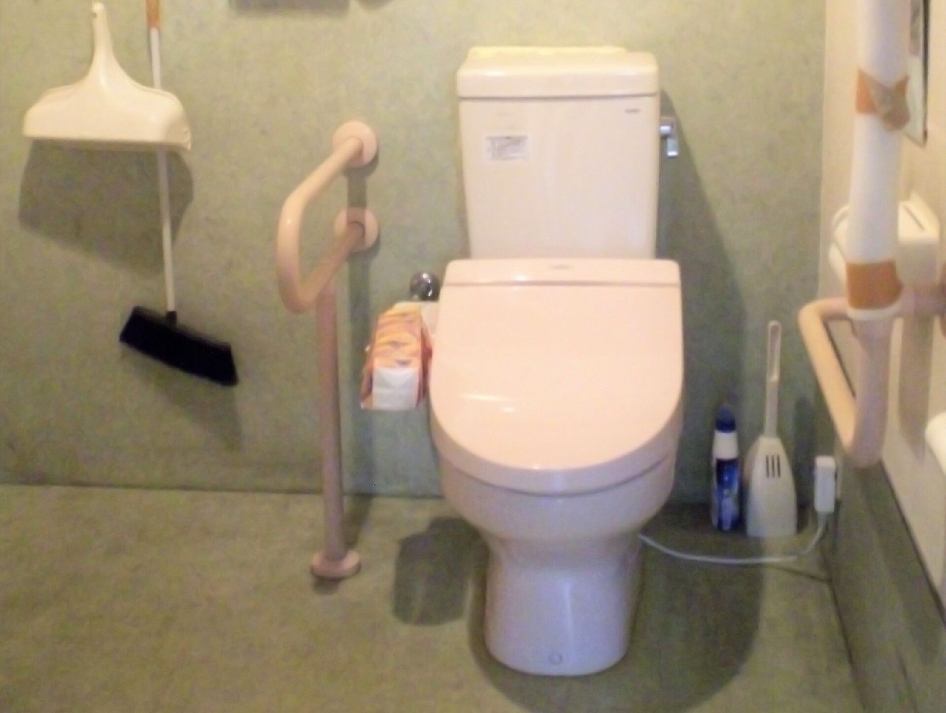 掃除用具や手すりが設置されている、ピンク色の温水洗浄便座