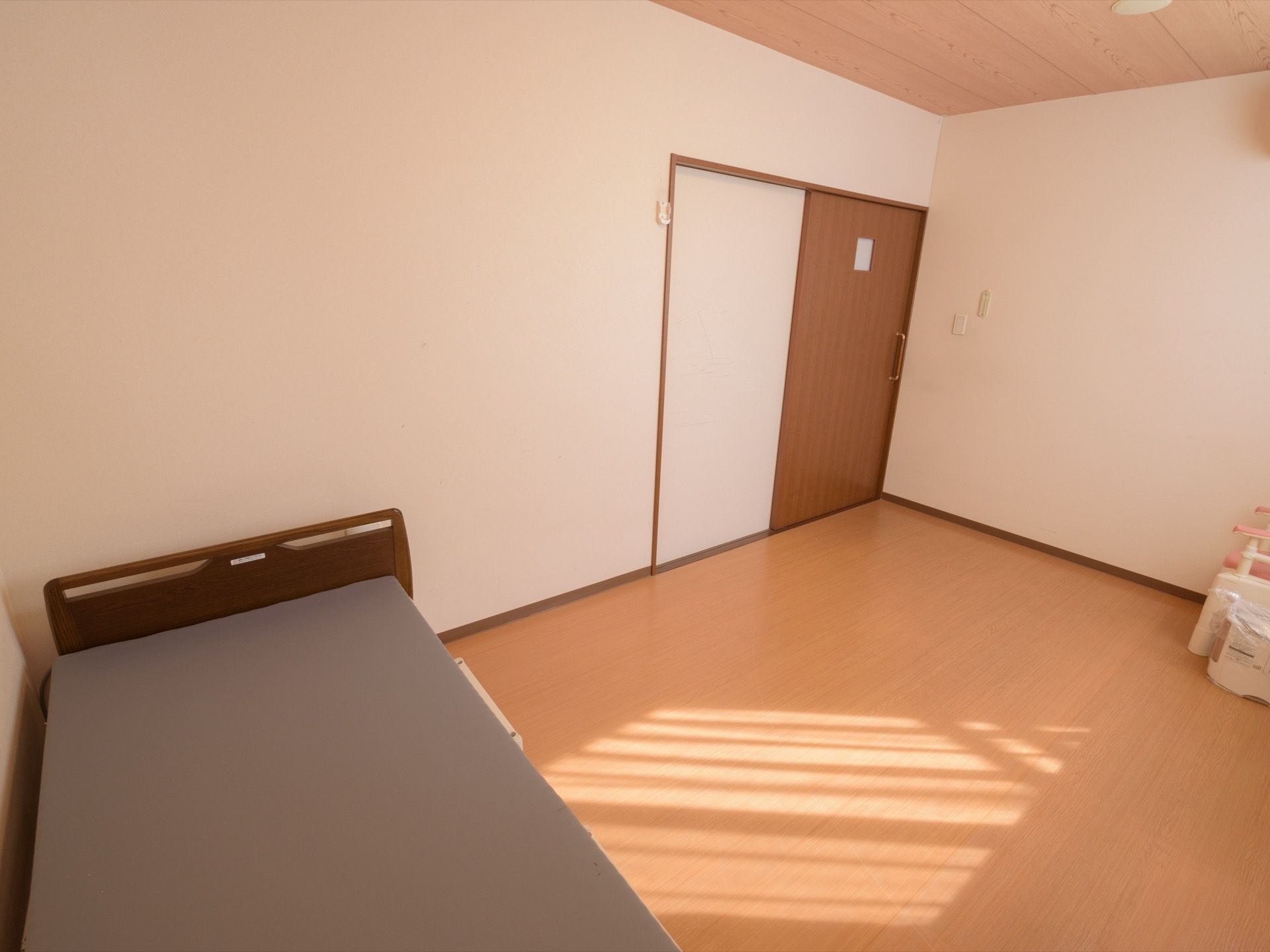 居室には広々としている。グレーのマットが乗ったベッドが設置されている。ピンクのひじ掛けが付いた椅子のようなものもある。