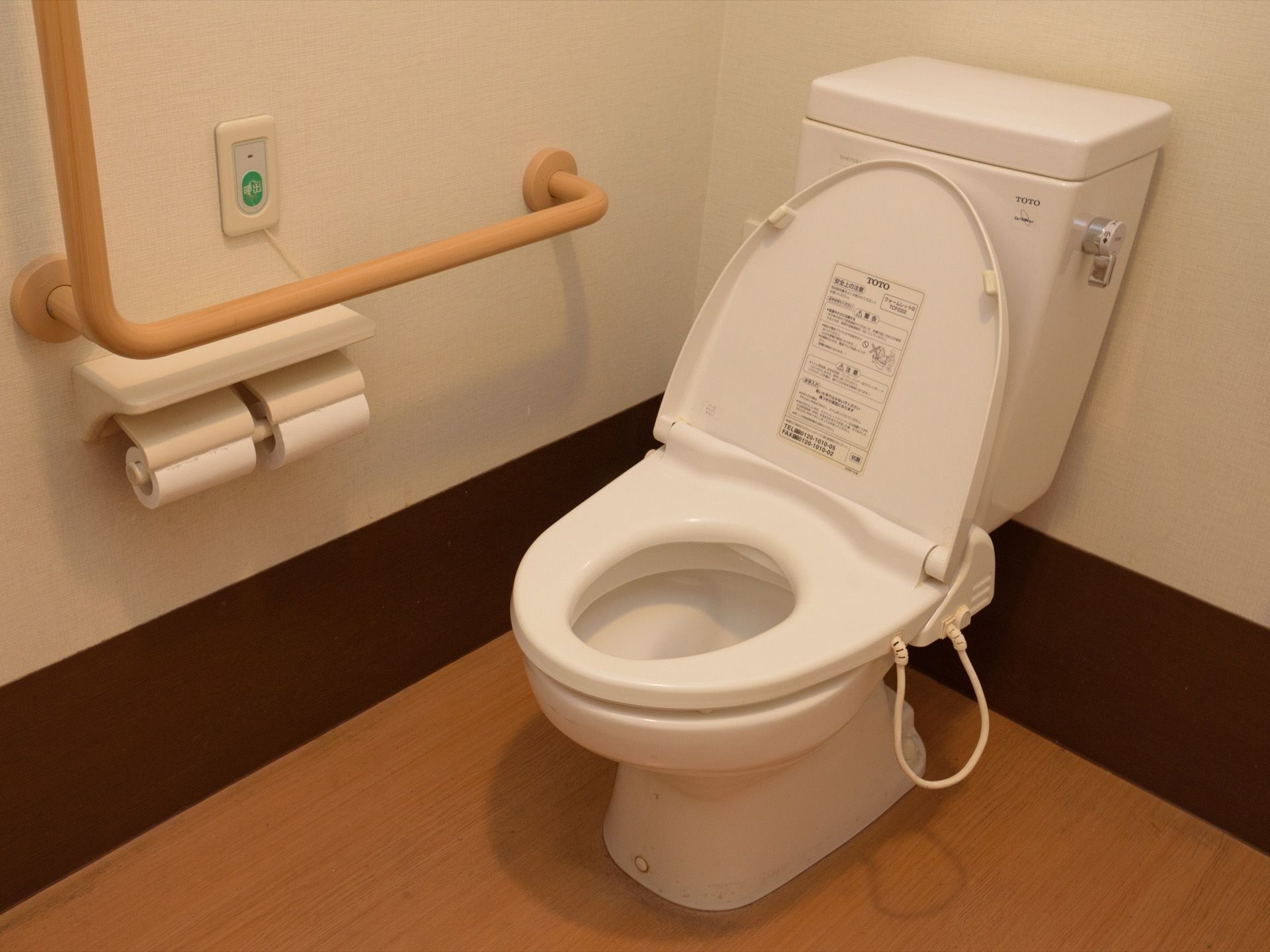 トイレには洋式便器が設置されている。片方の壁側には木製の手すりと呼び出しボタンが取り付けられている。