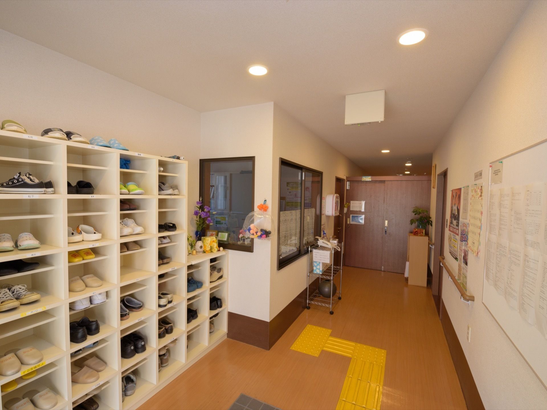 6段の靴箱が設置されている。隣にはガラス窓が取り付けられた部屋がある。窓の横の壁にはAED装置が取り付けられている。
