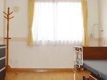 室内にフェンス付きの介護ベッドが設置されている。向かい側には洋服ダンスやポールハンガーが置かれている。