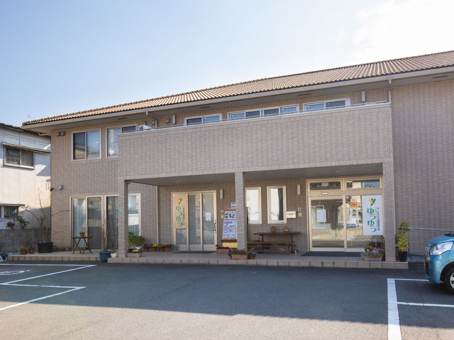 ベージュの外壁にオレンジの洋瓦の建物である。２階建てで、玄関の上には大きなバルコニーが造られている。