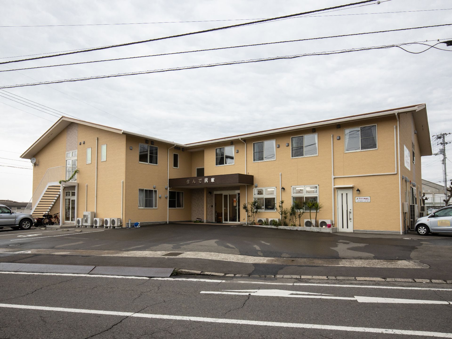 ベージュ色の外壁が集合住宅のような見た目である。玄関前まではお車で来ることができるように、広いスペースが確保されている。