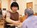 明るく温かな雰囲気の部屋で、女性スタッフが男性入居者様とテーブルで将棋を指している。時計が壁に設置されている。