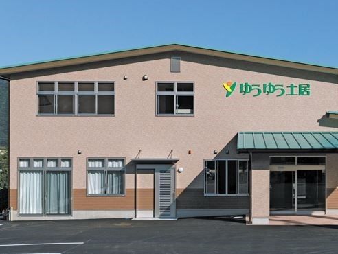 アスファルトで舗装された敷地に２階建てのベージュ色の壁の建物がある。２階の壁面に緑色の文字で施設の名称が表示されている。