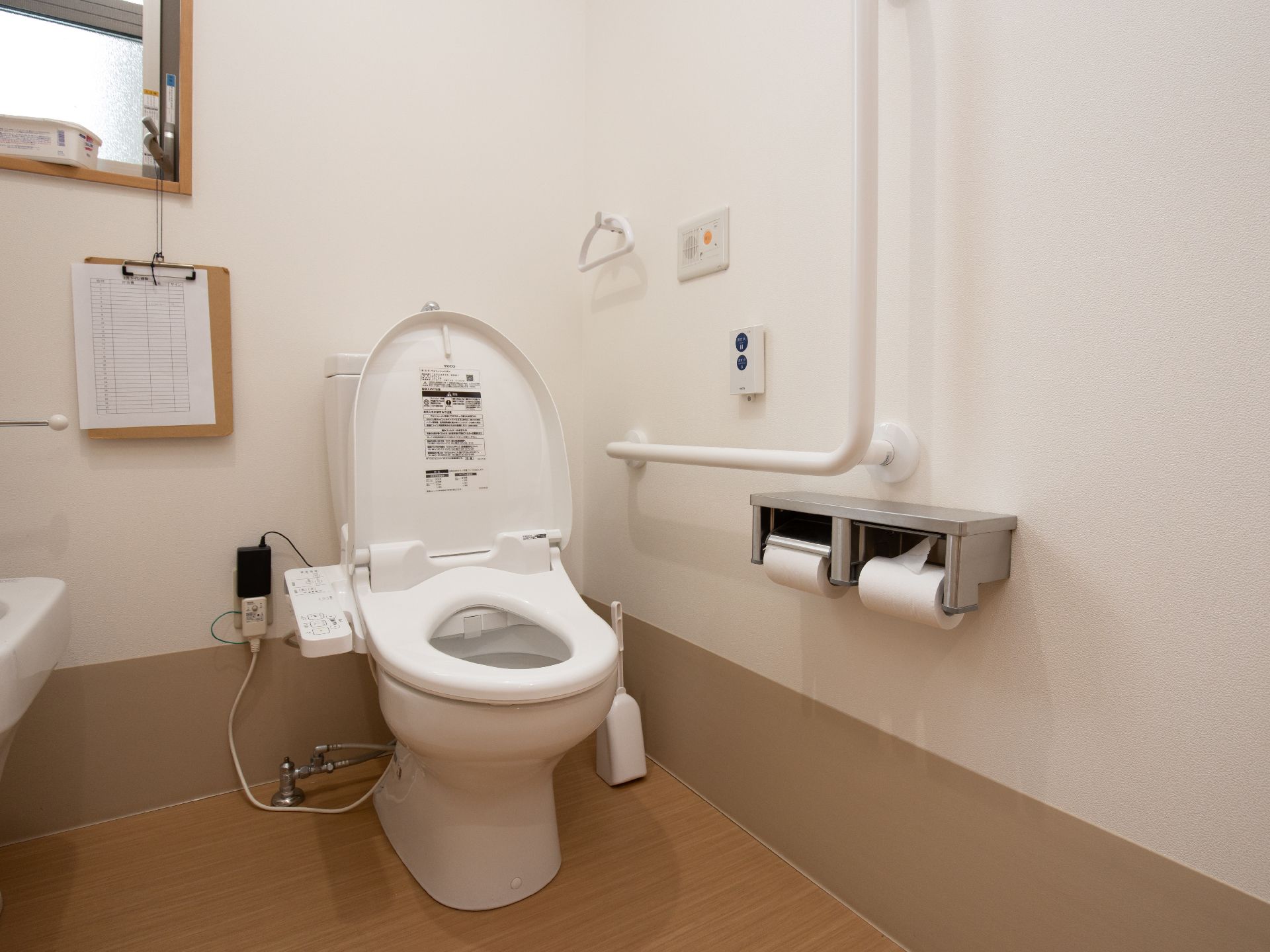トイレの壁は白、床は木目調のフローリングを採用している。壁には手すり、緊急通報装置が設置されている。