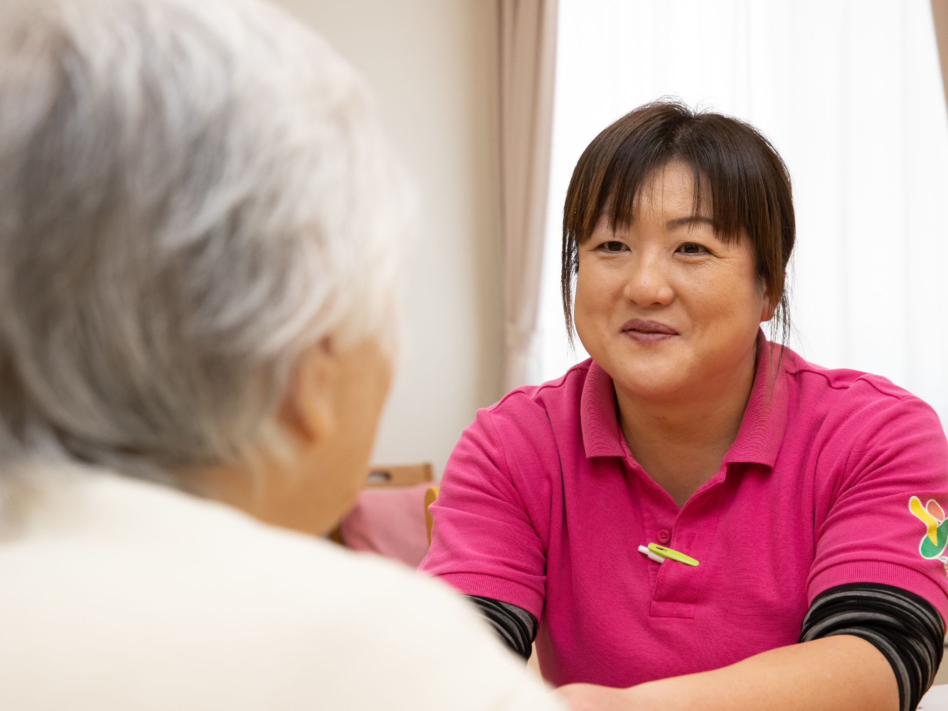 女性スタッフが入居者様に笑顔で談笑している。生活のサポートだけではなく、一人一人とコミュニケーションを大切にしている。