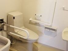トイレには洋式便器が設置されている。便器の横には可動式の手すりが設けられている。壁にも手すりがある。