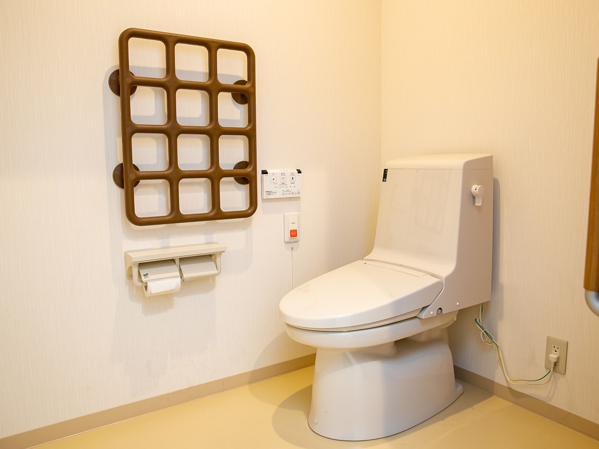 ゆとりあるスペースに洋式トイレが設置されている。ブラウン色の格子状の手すりがあり、つかまりやすくなっている。