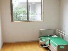 緑色のマットレスが載ったベッドが壁際に置かれている居室