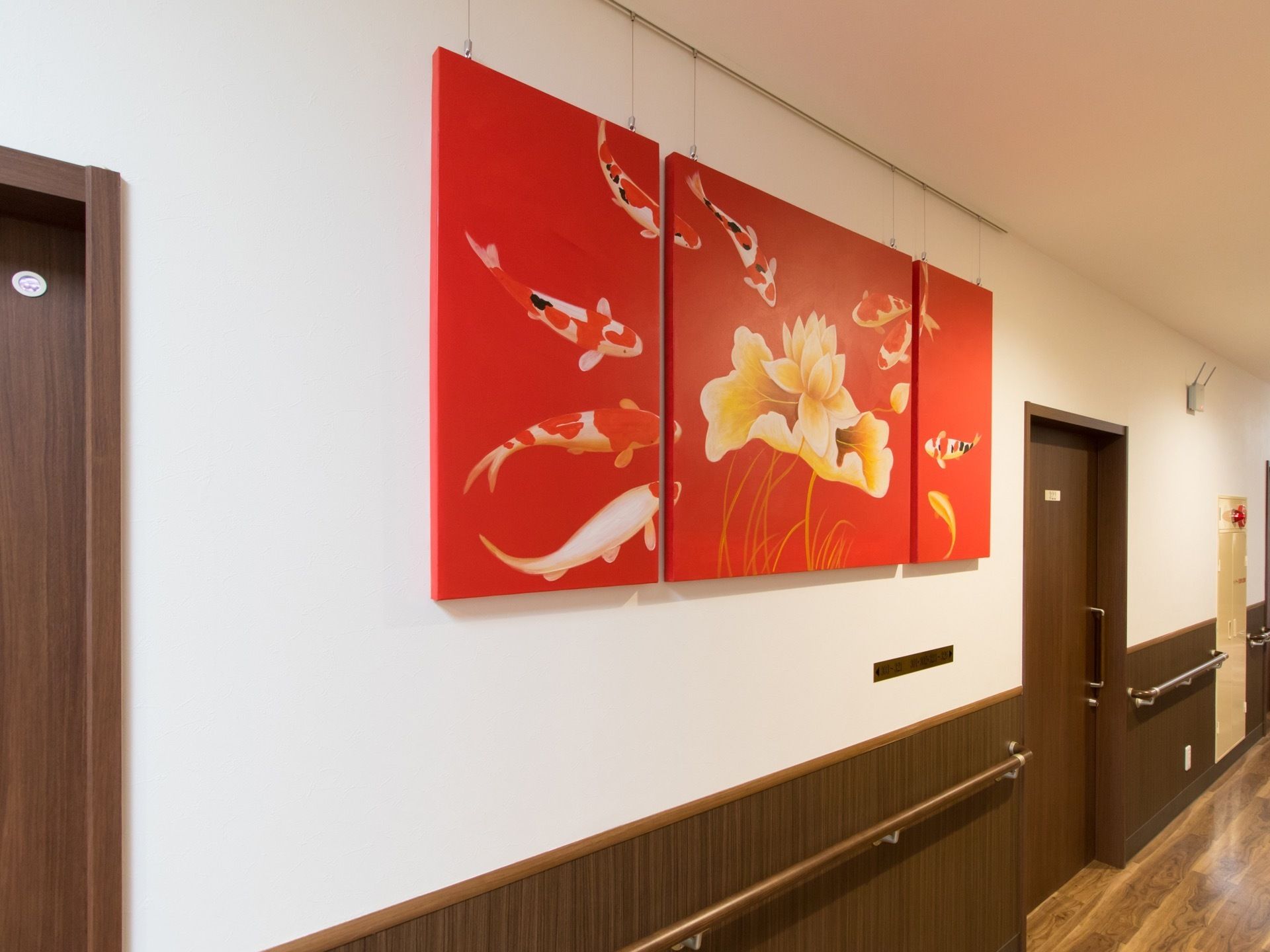 廊下の壁に、大きなパネルアートが飾られている。赤がメインの明るい色を使った絵である。また奥には消火栓が設置されている。