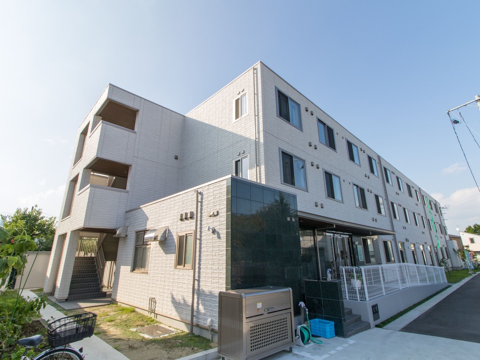 玄関前にはスロープが設けられており、その脇に白いフェンスが付いている。建物の左側に、幅の広い階段がある。