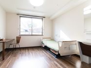 洗面台、電動介護ベッド、机と椅子が置かれている1DKの居室である。洗面台の上には鏡や照明が備わっている。