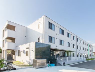 白い壁の３階建ての、横長の建物である。左端に幅の広い階段がある。玄関前には階段とスロープが設けられている。