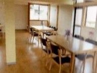 窓が多く明るいリビングには、テーブルと椅子が並べられている。椅子は座面と背当て部分が黒色で、テーブルの中央には花が飾られている。