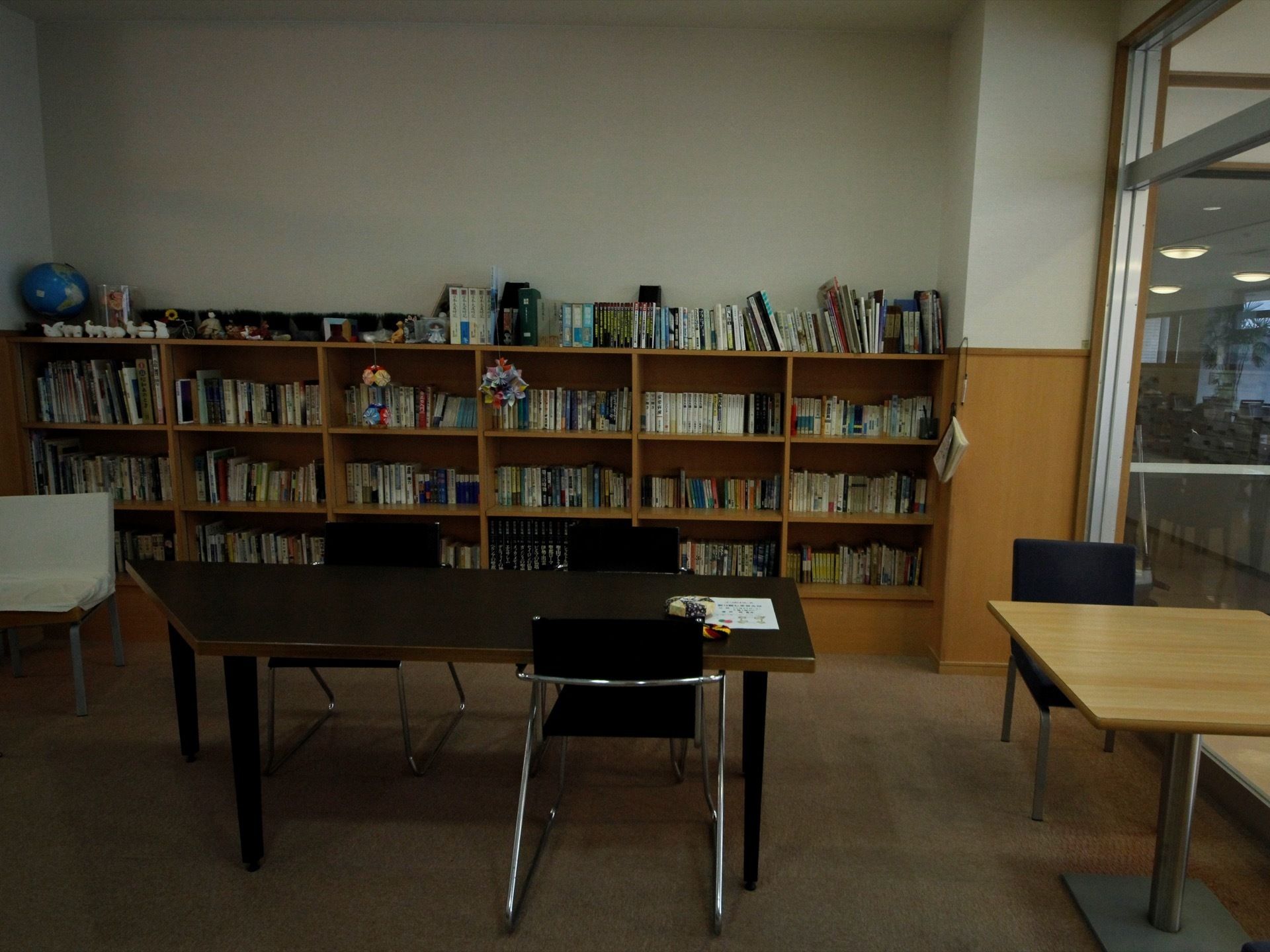 本棚にたくさんの本が入れられている。その手前にはテーブルや椅子が置かれている。本棚の上に地球儀や小物も載っている。