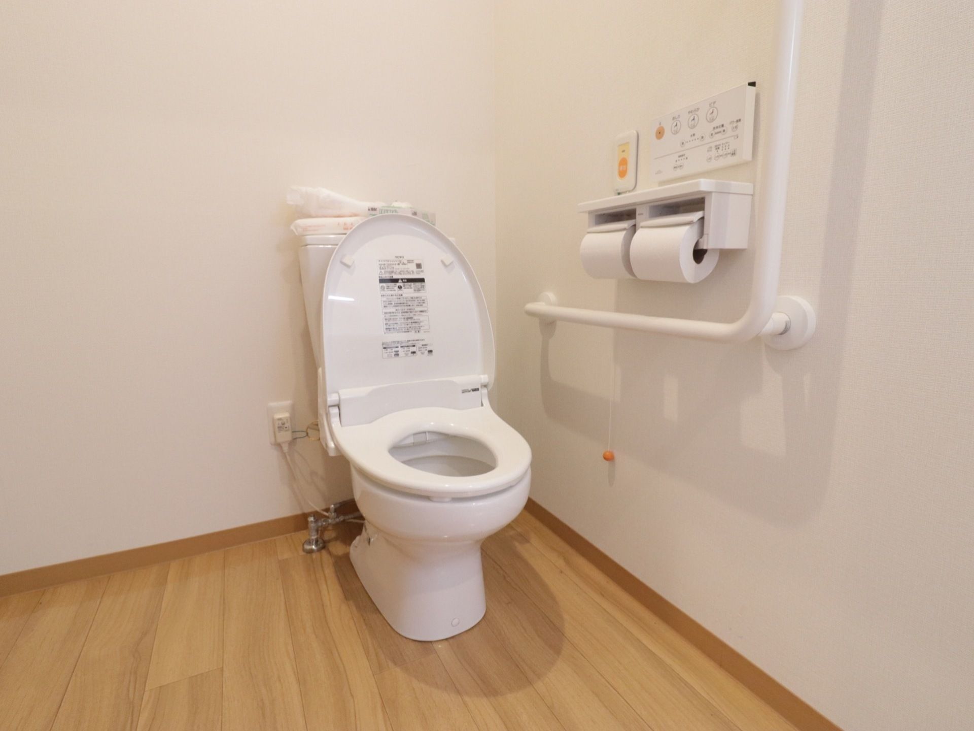 それぞれの居室にはトイレが備え付けられている。温水洗浄便座のコントローラーが手すりと共に壁に取り付けられている。