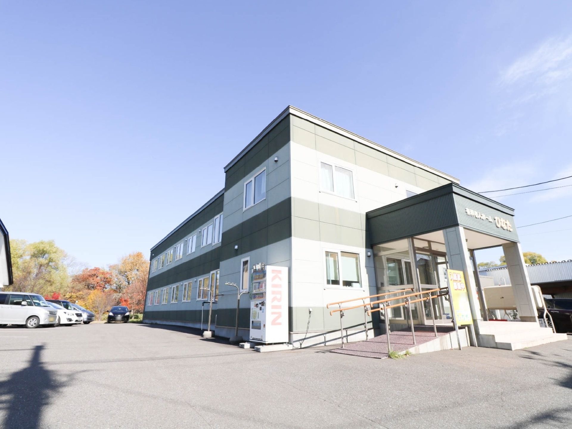 建物の周りは、アスファルトで舗装された広い敷地になっている。駐車スペースには車が４台停められている。