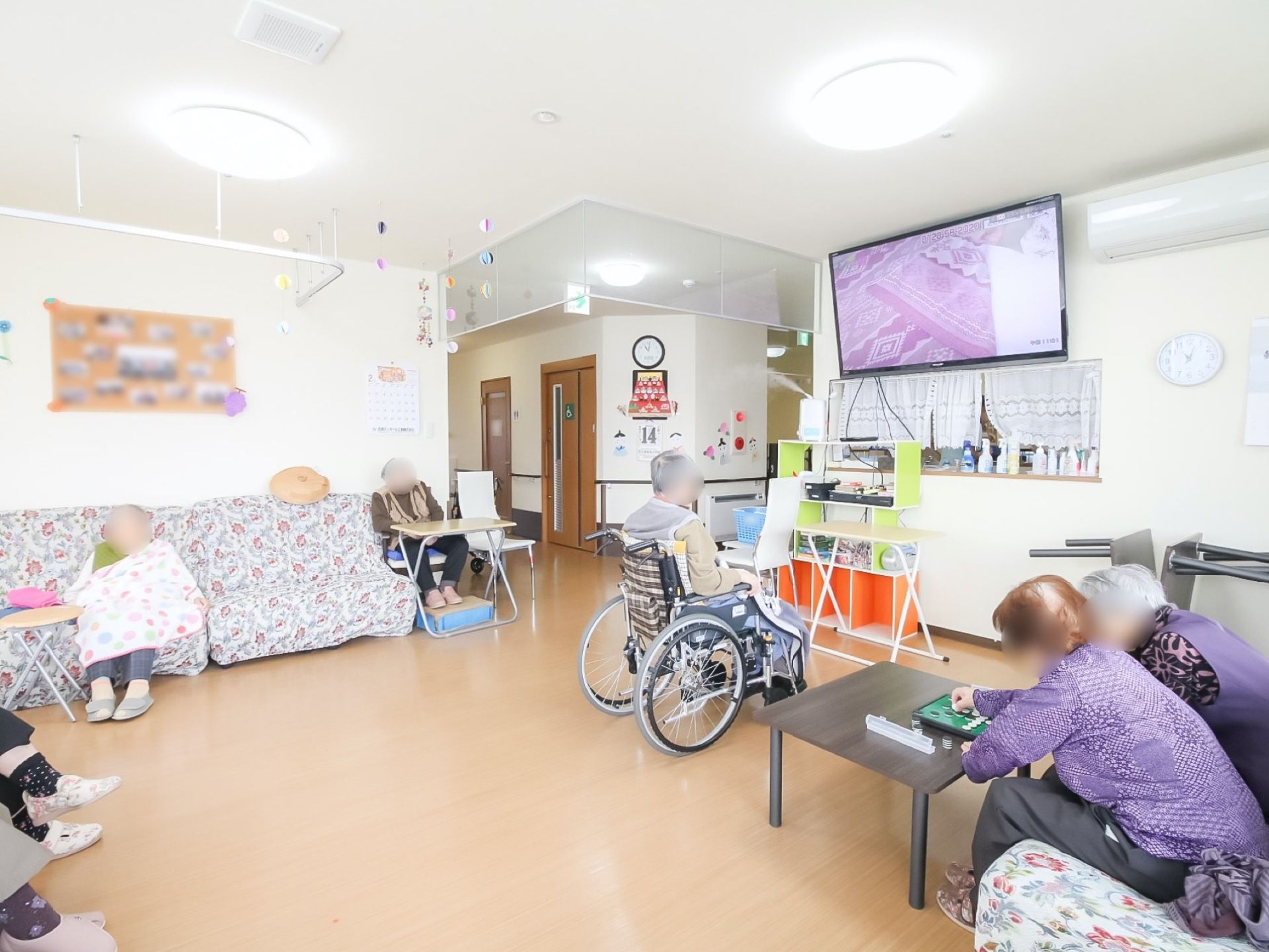 リビングはとても広く、開放的である。大型の壁掛けテレビがあり、遠くからでもよく見える。入居者様が大勢くつろいでいる。