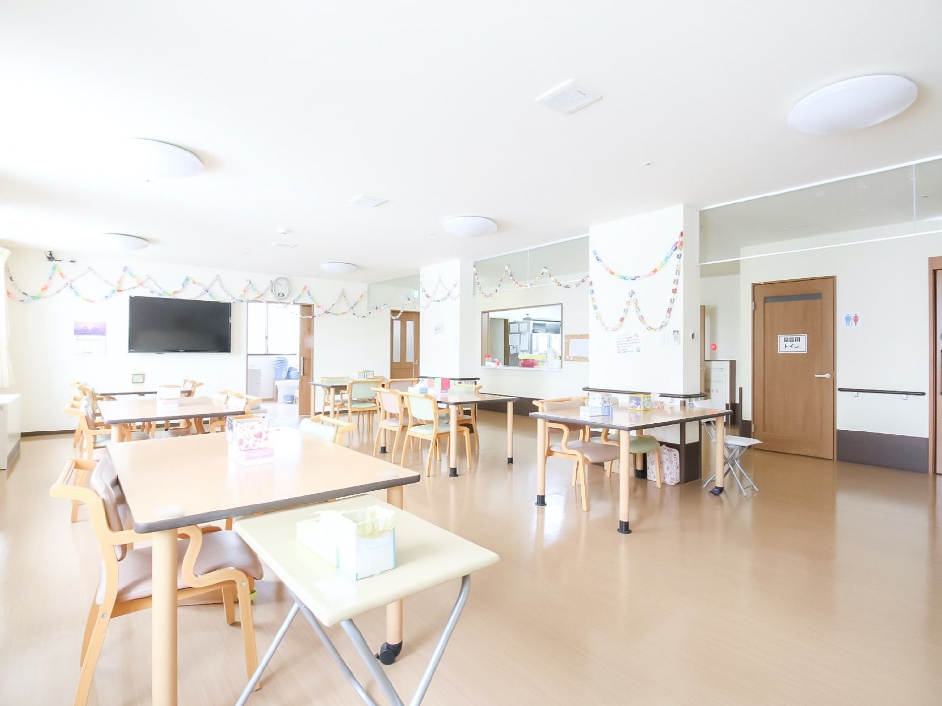 天井が高く、広々とした食堂にダイニングテーブルが置いてある。廊下とひと続きになっていて開放感がある。壁面に輪飾りが掛かっている。