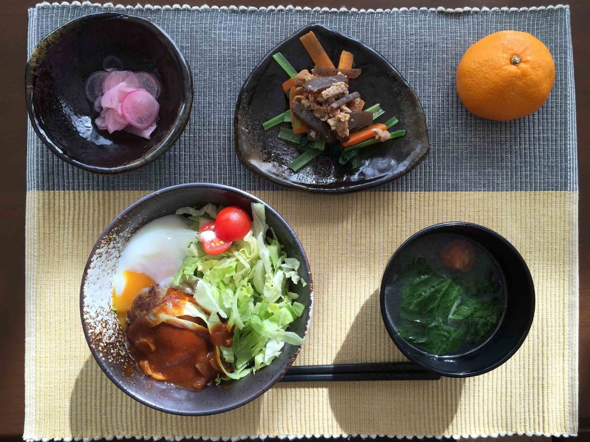 丼にサラダ、汁物、みかんなどがランチョンマットの上に並んでいる。食べやすく栄養バランスを計算している食事なので安心して食べることができる。