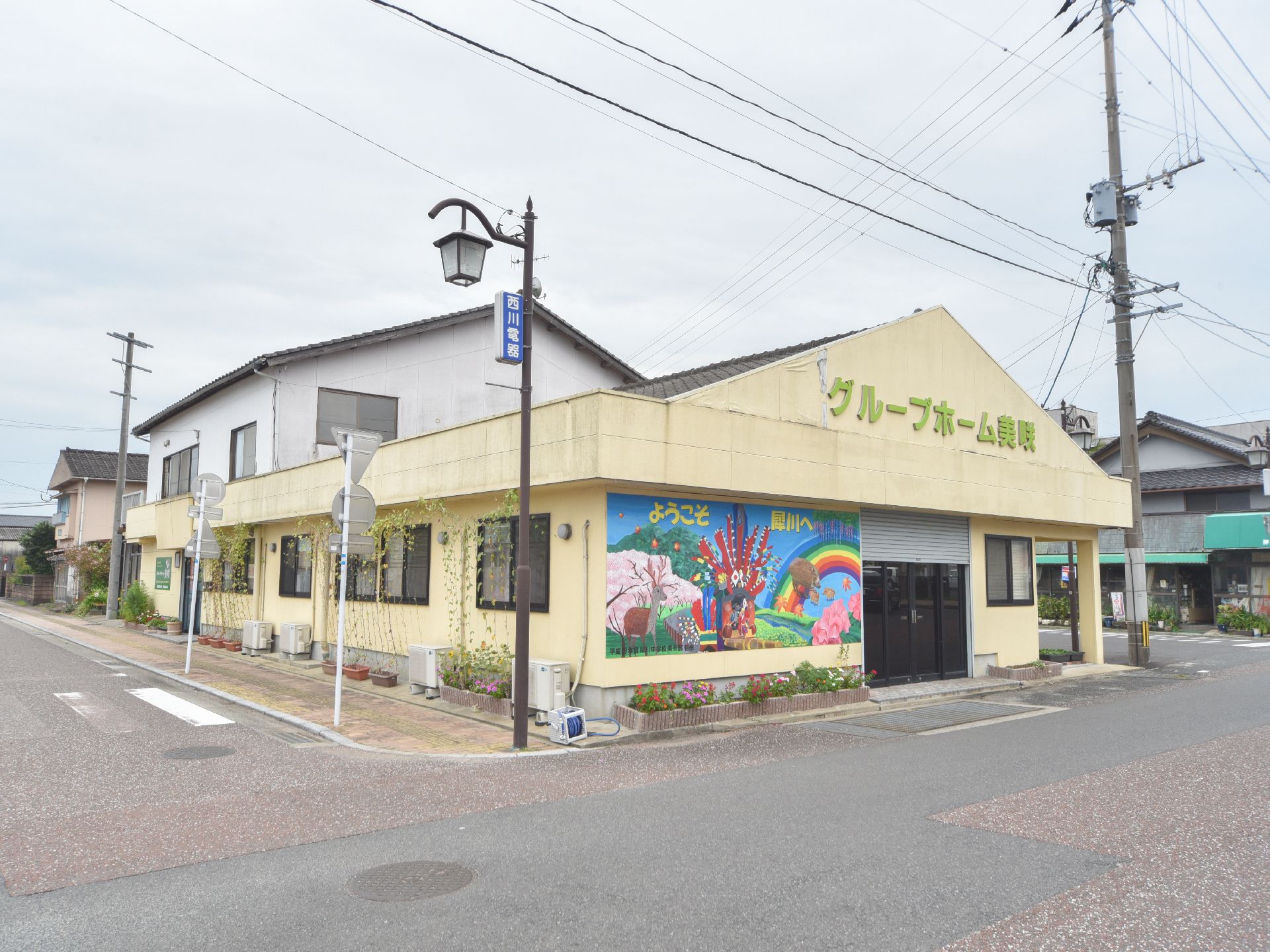 住宅街の角地に立地している施設の外観。クリーム色の外壁と入り口の壁に描かれた絵が明るい雰囲気の施設。