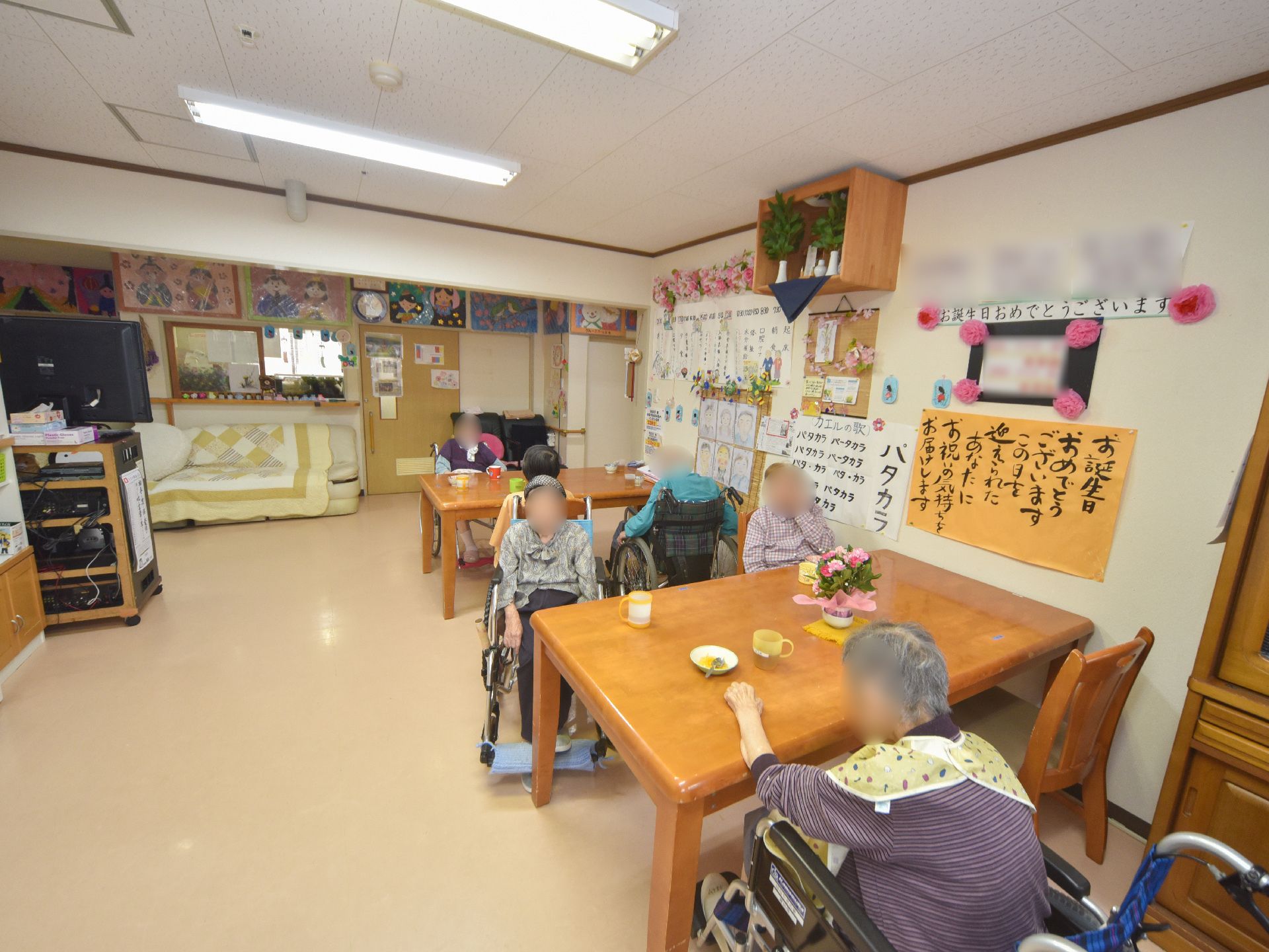 2台の大きめのテーブルがゆったりとした間隔で配置されている共有フロア。テレビやソファも置かれている。
