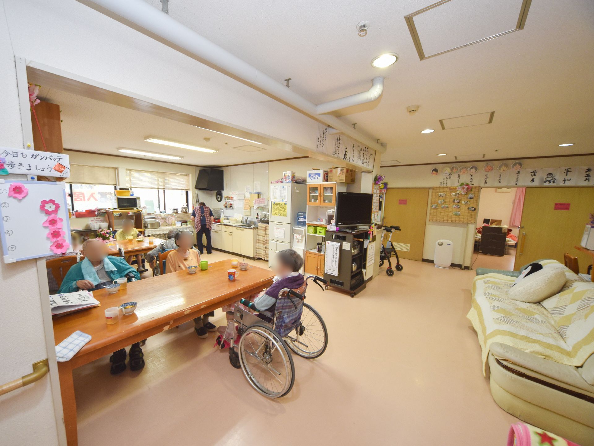椅子や車いすに座って、食堂のテーブルについている入居者様たち