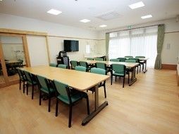 入口はバリアフリーでスライドドアである。広く明るい部屋にはテーブルセットが並び、テレビやエアコンもある。