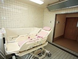 落ち着いた色の広い浴室にはリフト入浴機がある。脱衣所も広く入口はバリアフリーである。大型空調機があり清潔である。
