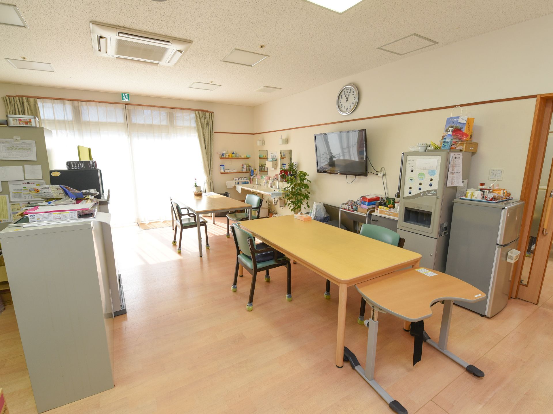 壁側に給水機や冷蔵庫が並べて置かれている。天井には四角い形の埋め込み式のライトが取りつけられている。