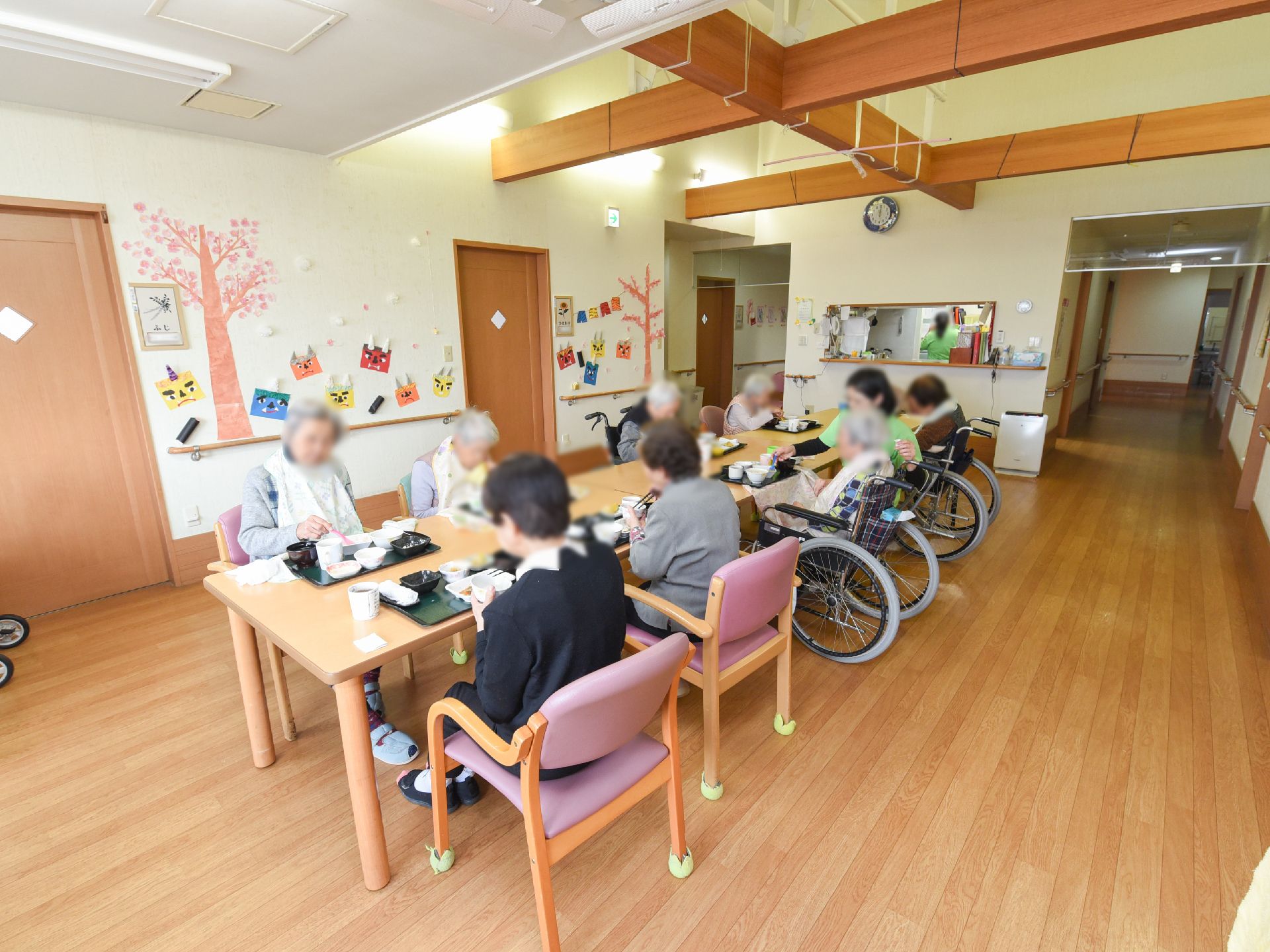 ２つのテーブルが並べて置かれていて、食事を摂っている。車椅子のままの入居者様と椅子に座っている入居者様がいる。
