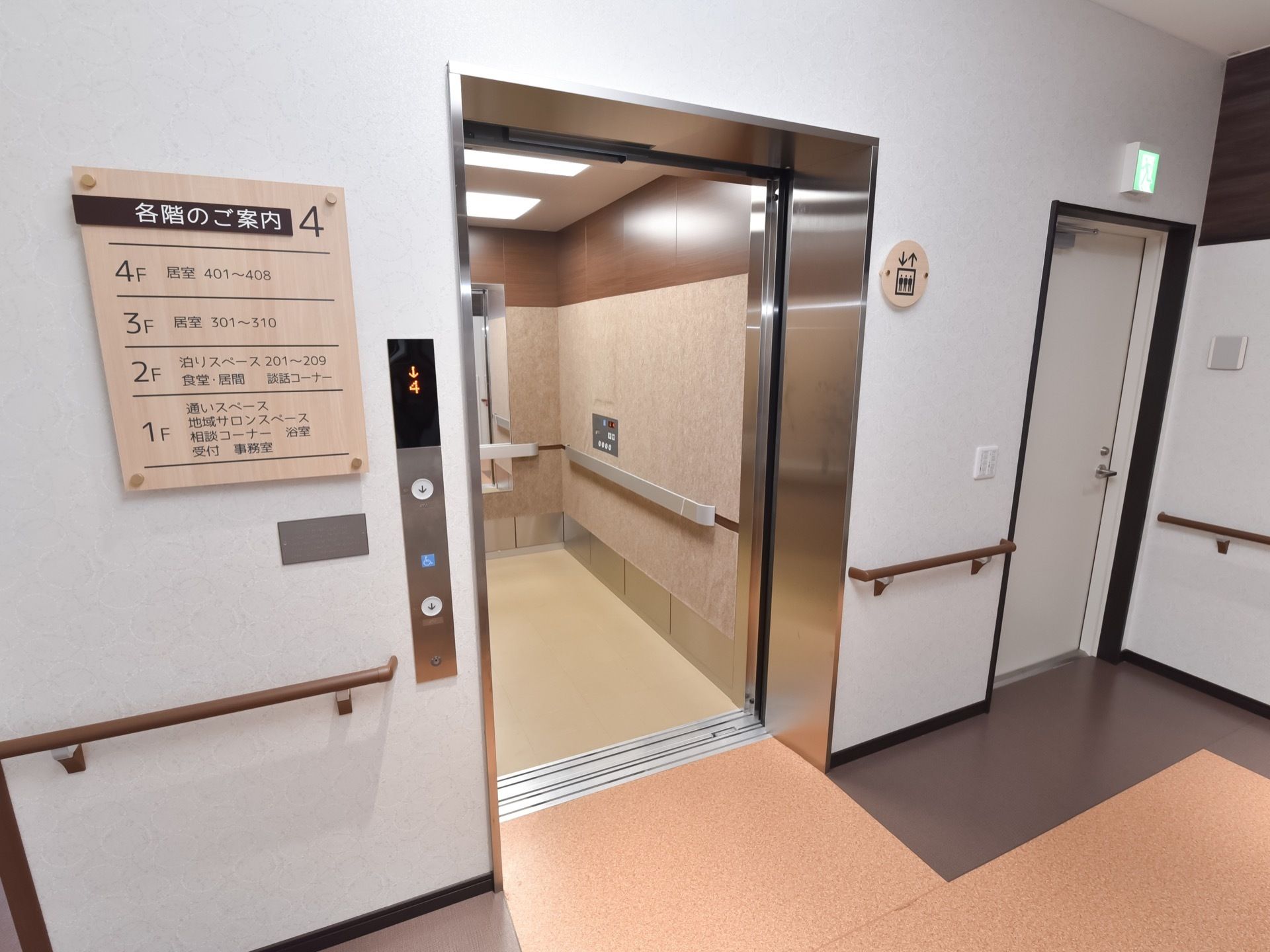 施設内に完備されているエレベーターである。壁には、エレベーターの表示マークや「各階のご案内」が設置されている。