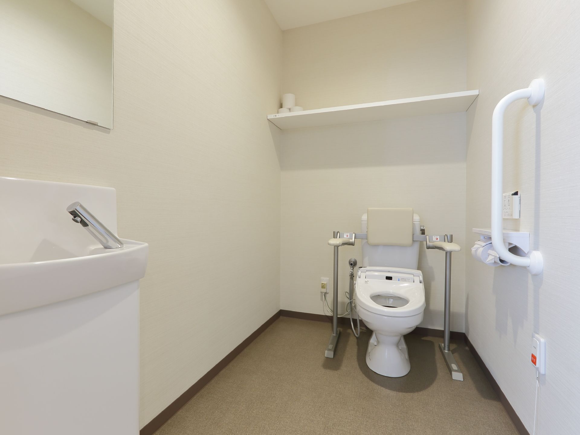 清潔感のあるトイレである。便器には背もたれがあり、安心して腰を掛ける事が出来る。壁には手摺が付けられている。