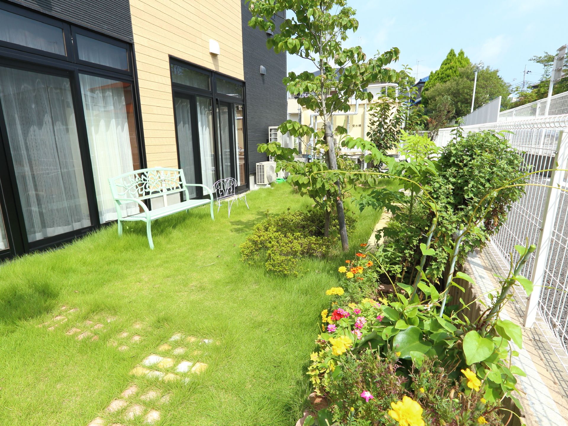 施設には建物の前に芝生が植えられた庭が設けられている。外周には白いワイヤーのフェンスがあり、内側には花が咲いている。