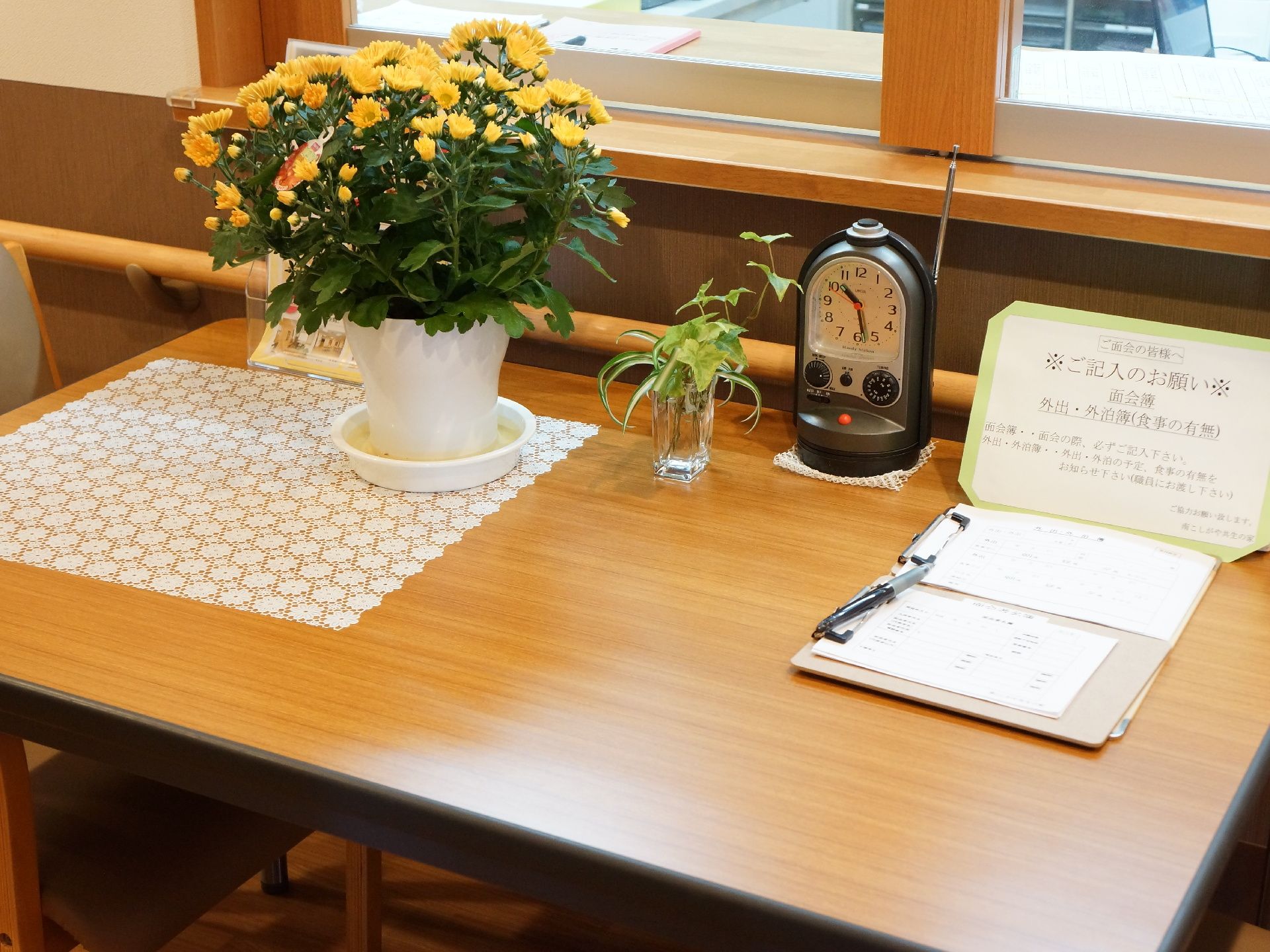記帳台の置かれた小さなデスク。ここで面会者や入居者様の出入りの記録を管理する。また手を消毒するスプレーが置かれている。