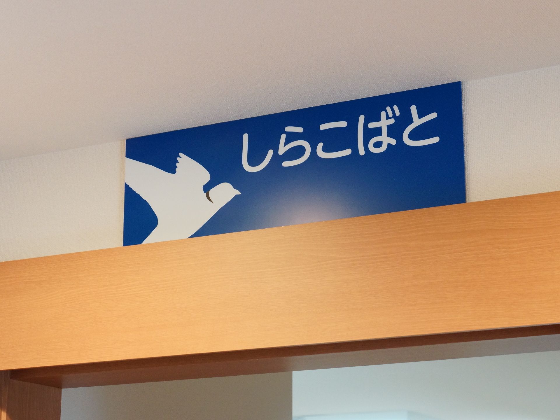 廊下の壁と天井は白で統一されている。部屋の扉の縁には明るいブラウンの木材が使われている。青いプレートが付いている。