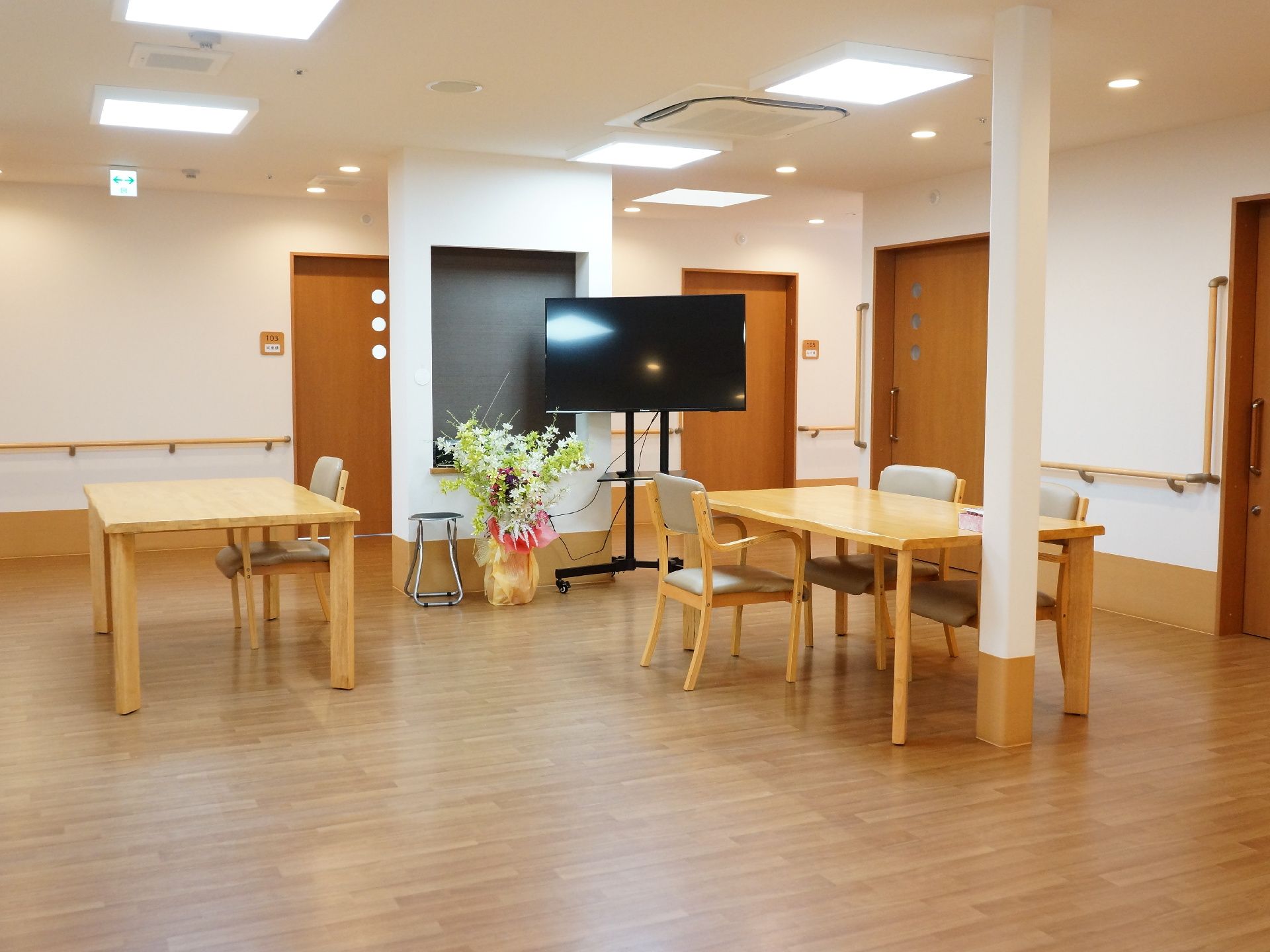 ラッピングされた豪華な花瓶の隣には非常に大型のワイドテレビが設置されている。台はキャスターになっており移動可能。
