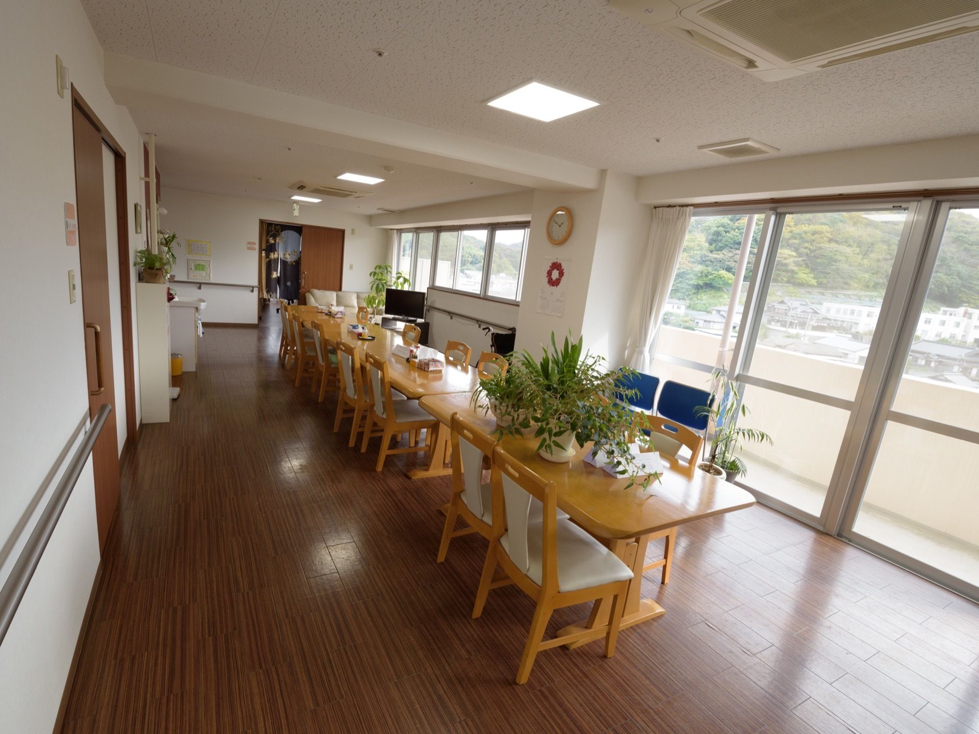 大きな窓がある明るい食堂。床はフローリングになっていて、テーブルを囲むようにたくさんの椅子が置かれている。
