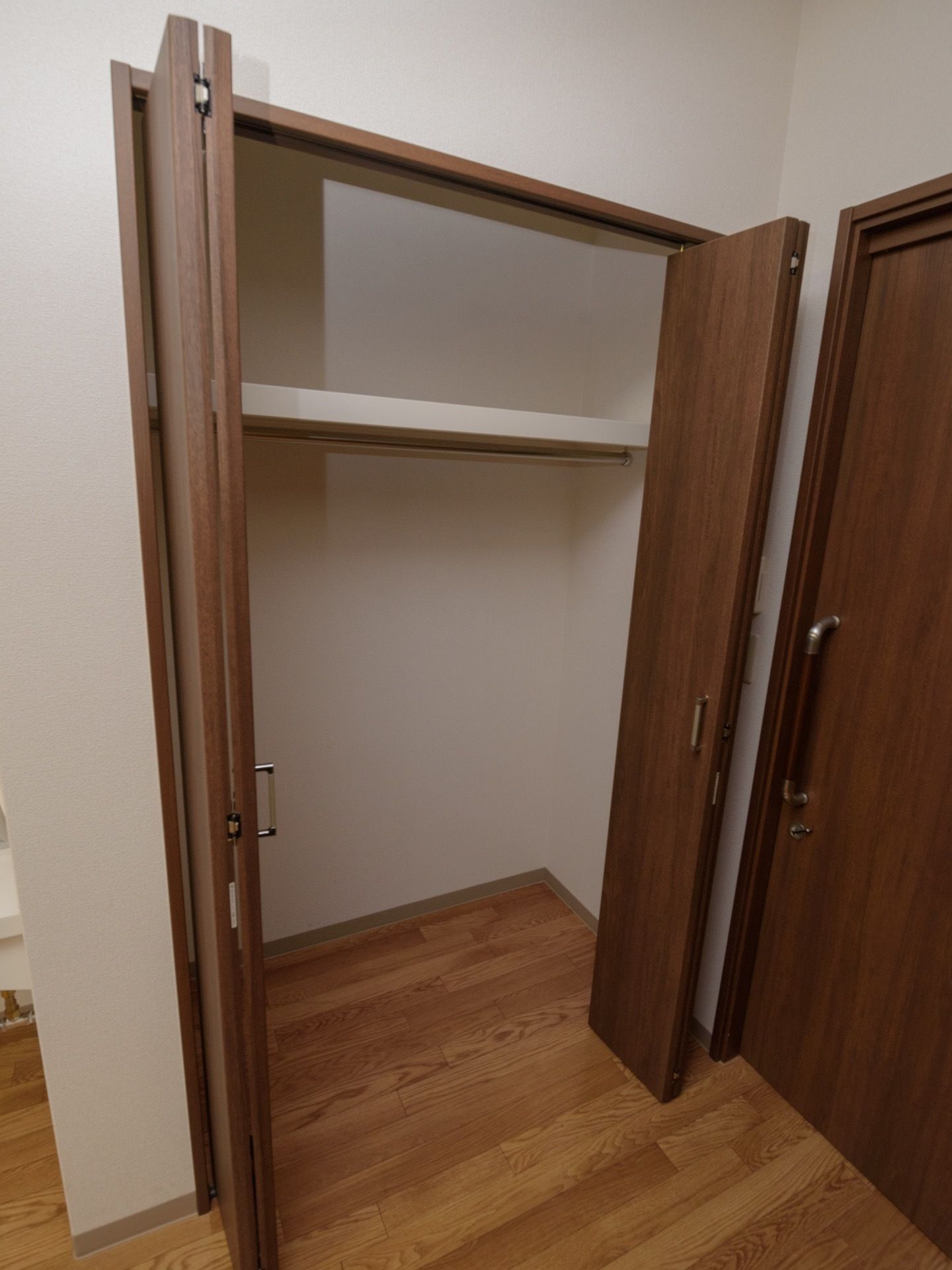 室内の入口ドアの近くに、クローゼットがある。茶色い開き戸のクローゼットで、上に棚があり下にポールがついている。