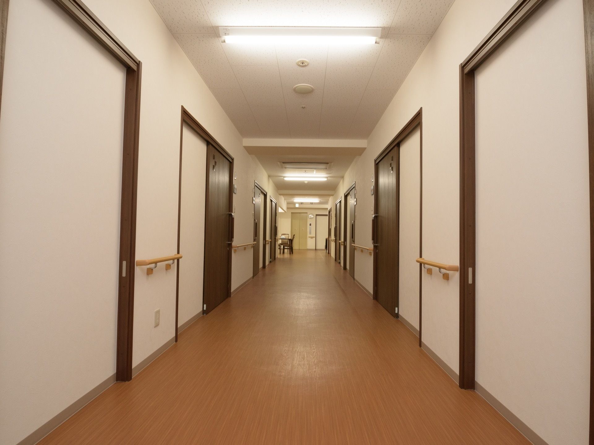 廊下がまっすぐ伸びている。壁と天井は白色で、居室ドアと床は茶色である。床はフローリングで、壁に手すりが付いている。