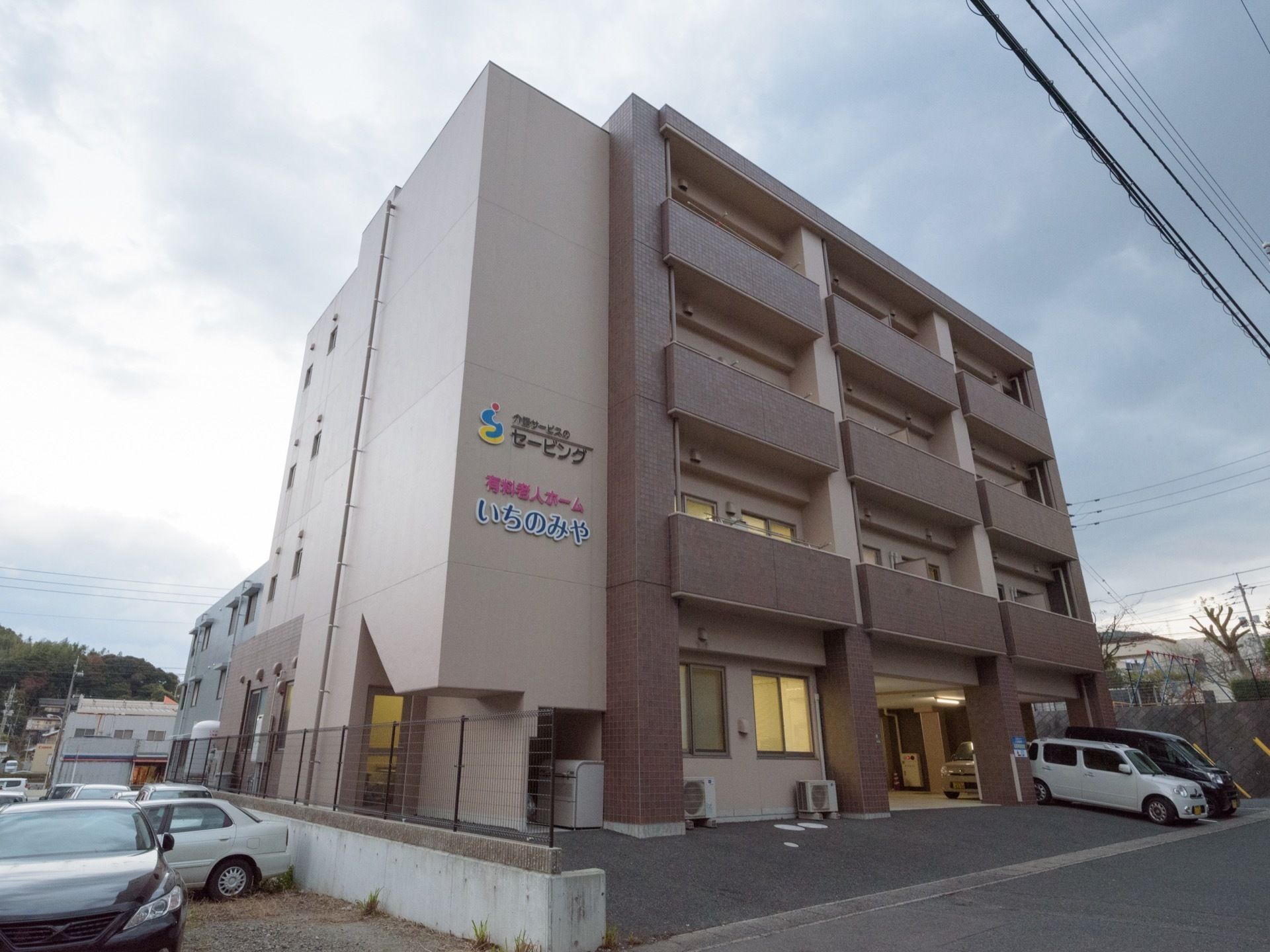 施設の建物は4階まである。1階はオープンになっており、車が数台停まっている。建物に大きく施設名が表示されている。